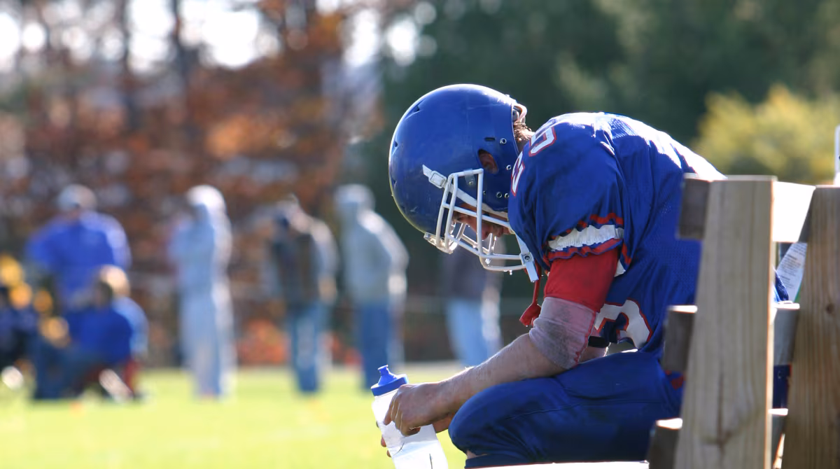 — title missing — Football player resting on bench with head down