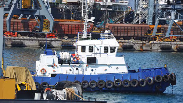 Tugboat and port cargo cranes. Credit: iStock / Getty Images Plus