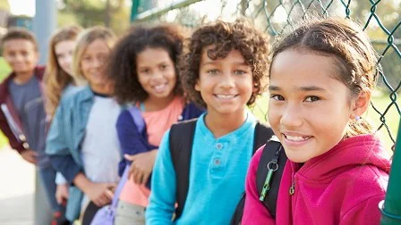 Smiling children with backpacks School-aged children lean against a fence and smile together.