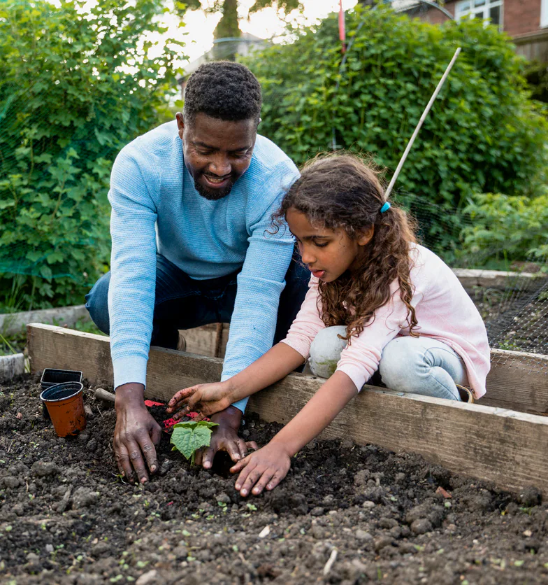 You're Doing So Well! An adult is helping a child plant in the garden.
