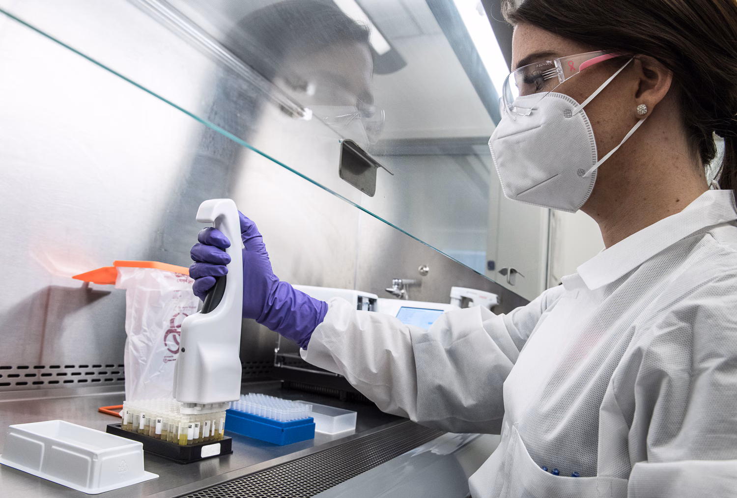 24502 A scientist wearing Biosafety Level 2 PPE gear including gloves, laboratory coat, goggles, and mask, while pipetting inside a Biological Safety cabinet (BSC).