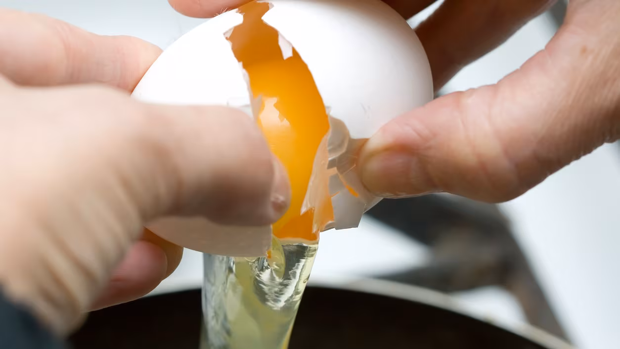 Hands cracking open an egg over a bowl.
