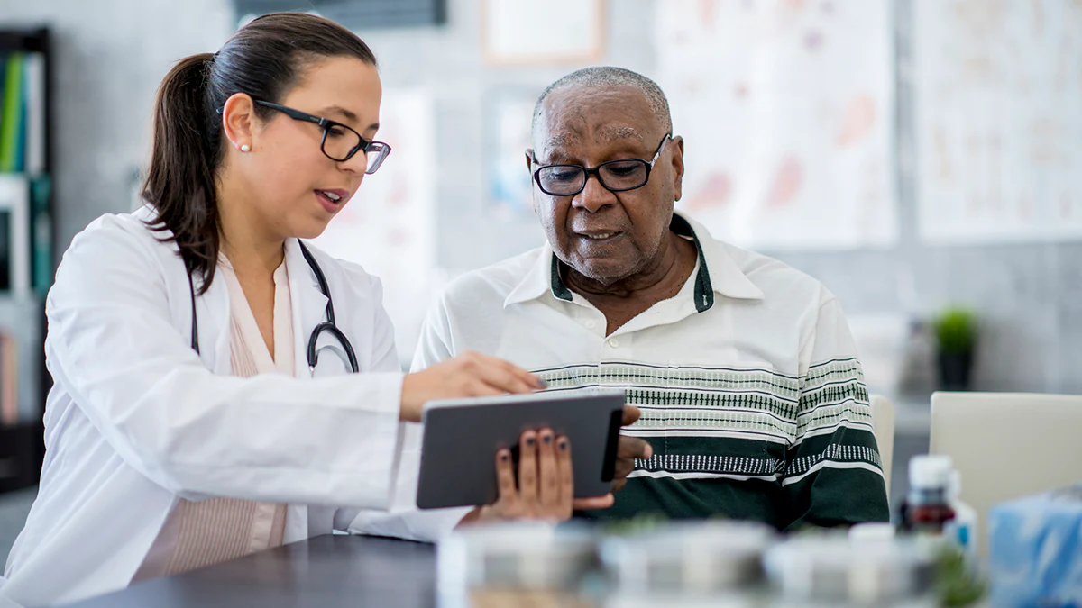 Doctor With A Tablet Computer White female doctor with brown hair in a low ponytail with Black older adult patient looking at a tablet.