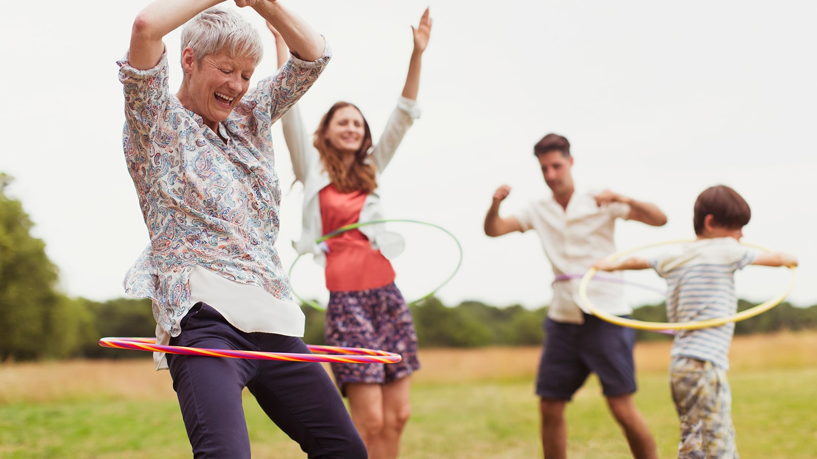 Playful multi-generation family spinning in plastic hoops in field Playful multi-generation family playing with hula hoops outside.
