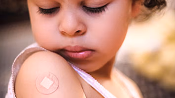A little girl looking at the band-aid on her right shoulder from where she got a vaccine.