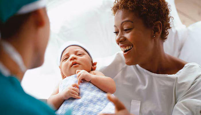 A mother smiles while holding her newborn baby in the hospital.