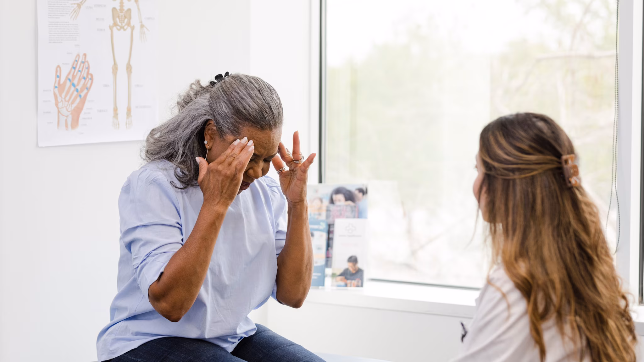 Older woman holding her head in pain in the doctor's office.