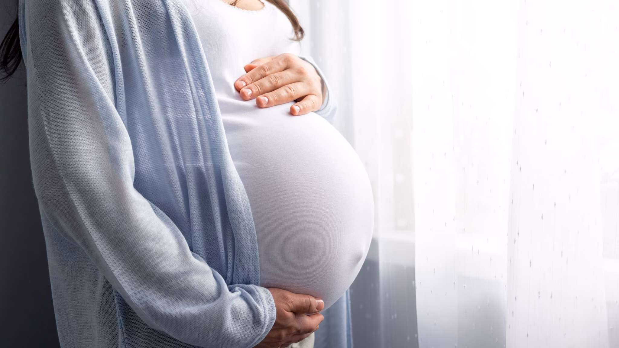 Pregnant person with hands on their abdomen.