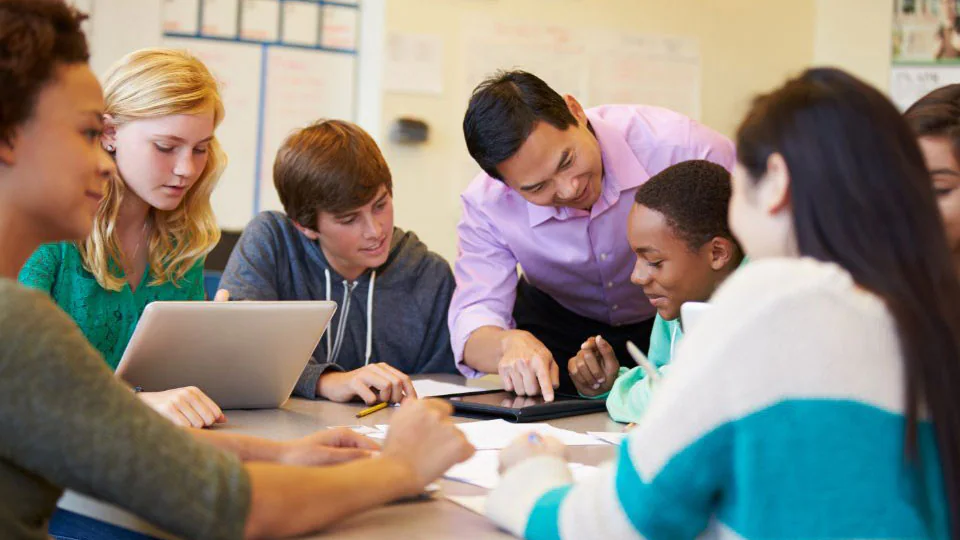 Classroom Management Students sitting around a table with two teachers reviewing schoolwork.