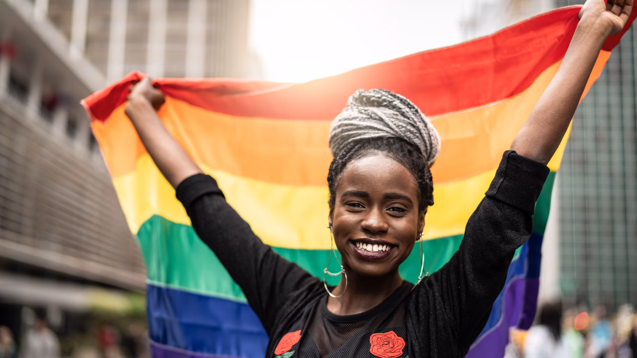 Inclusive practices Young woman holds up a rainbow flag behind her head.